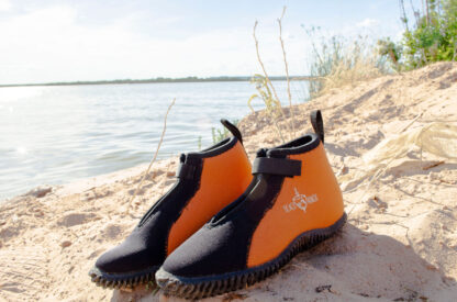 A pair of orange and black water shoes on the beach.